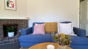 A living room with a blue sofa, a fireplace, and a wooden coffee table with a candle and flowers. - Cosy Flat metres from Rottnest Ferry (Fremantle)