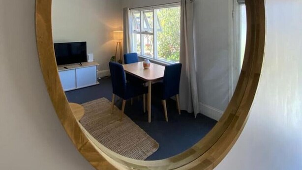 A room with a round mirror reflecting a dining area, a television, and a window with curtains. - Cosy Flat metres from Rottnest Ferry (Fremantle)