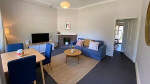 A living room with a sofa, coffee table, TV, fireplace, and a dining area with chairs and a table. - Cosy Flat metres from Rottnest Ferry (Fremantle)