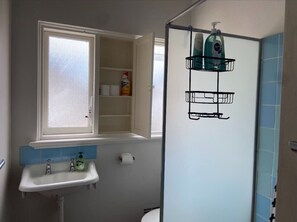 A bathroom with a window, a sink, a toilet, and a shower area.