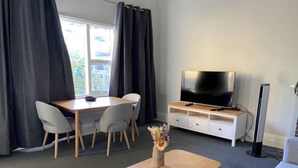 A modern living room with a wooden table, grey chairs, a flat-screen TV, and a small plant on a white cabinet. - Perfect Flat meters from WA Shipwrecks Museum (Fremantle)