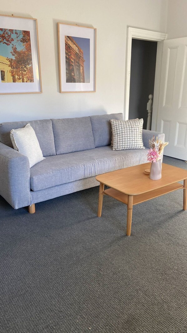 A living room with a grey sofa, two framed pictures on the wall, a wooden coffee table with a vase of flowers, and a grey carpet.