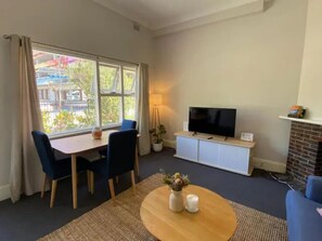 Una sala de estar con televisor, chimenea, mesa de comedor con sillas y ventana con cortinas.