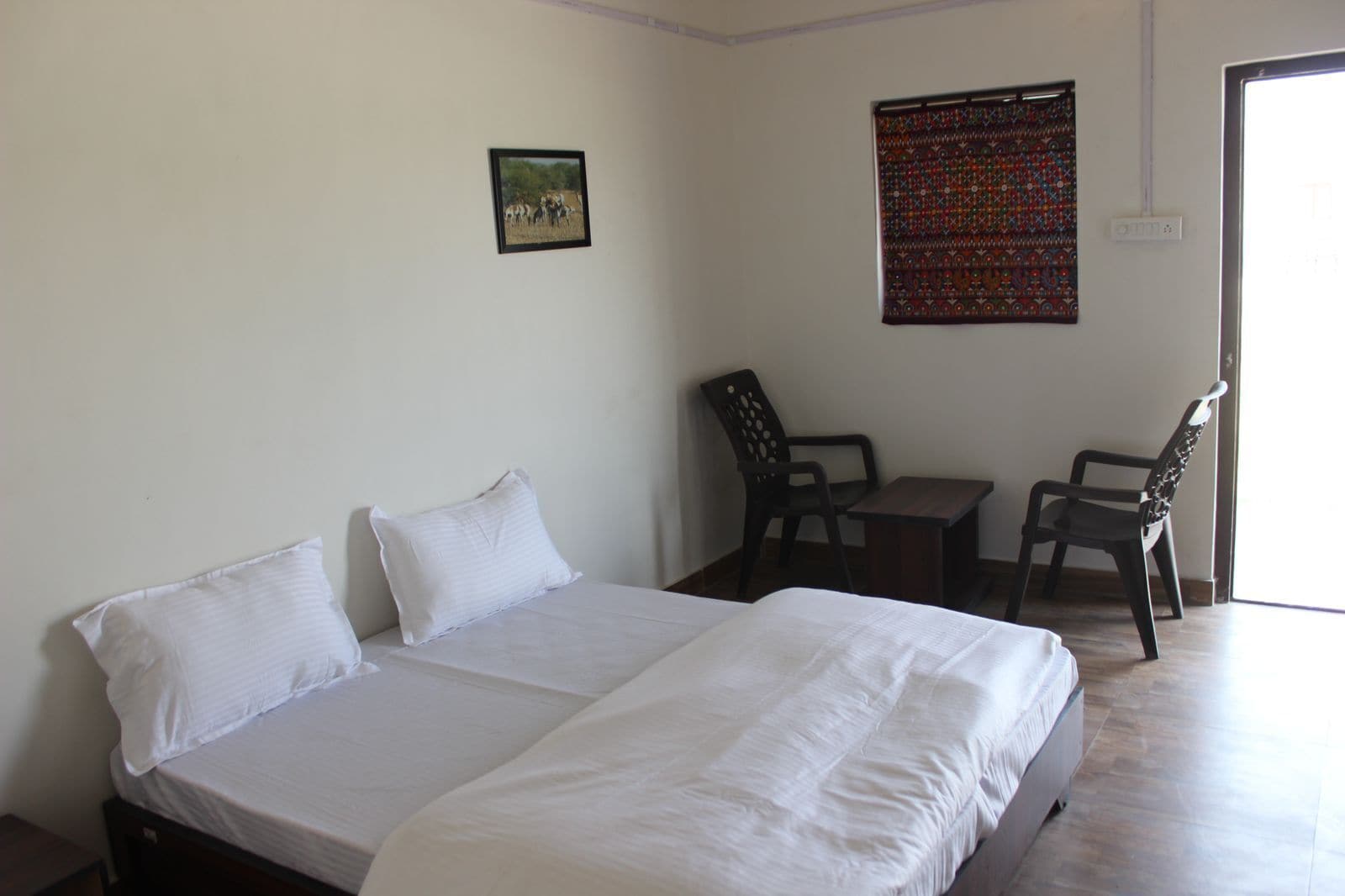 A room with a bed, two chairs, a small table, and a wall with a patterned tapestry.