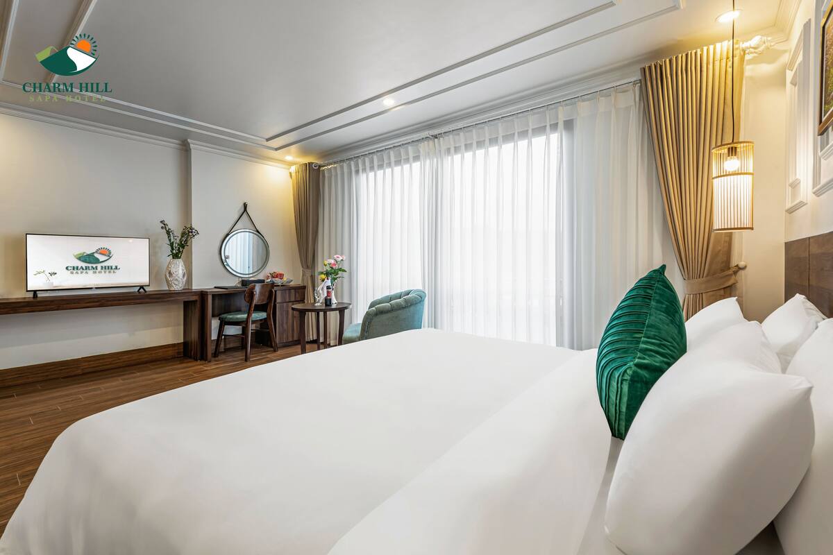A hotel room with a large bed, a desk with a chair, a TV, and a window with curtains.