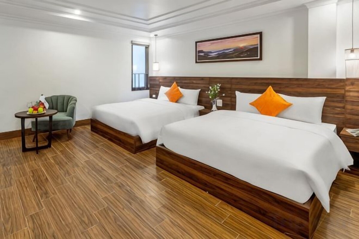 Een hotelkamer met twee bedden, een klein tafeltje met fruit, een stoel en een raam.