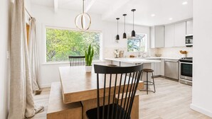 A modern kitchen with a dining area, featuring a large window, pendant lights, and a central island. - SlopeSide • Hot Tub • Arcade • Deck w BBQ+fire pit (Big Bear Lake)