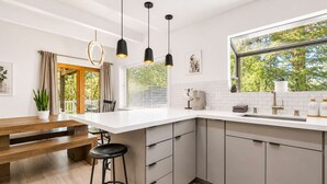 A modern kitchen with a white countertop, grey cabinets, a wooden bench, and a bar stool. - SlopeSide • Hot Tub • Arcade • Deck w BBQ+fire pit (Big Bear Lake)