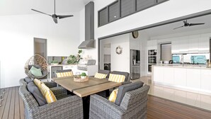 A modern kitchen with a central island, a dining area with wicker furniture, and a ceiling fan. - Belle Escapes 100 Cascade Palm Cove (Palm Cove)