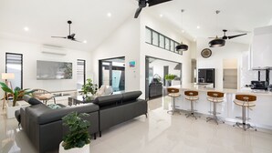 A spacious living area with a sofa, a dining bar with stools, a kitchen, and a ceiling fan. - Belle Escapes 100 Cascade Palm Cove (Palm Cove)