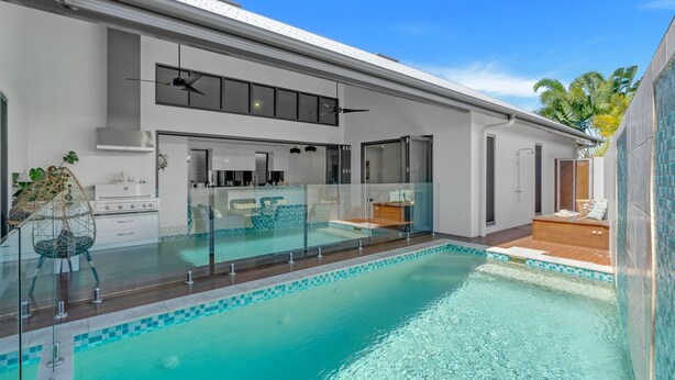 A modern house with a glass-enclosed swimming pool, a kitchen, and a dining area. - Belle Escapes 100 Cascade Palm Cove (Palm Cove)