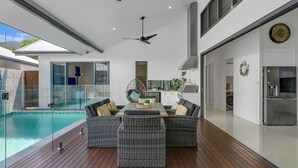 A modern outdoor living area with a pool, dining set, and kitchen. - Belle Escapes 100 Cascade Palm Cove (Palm Cove)