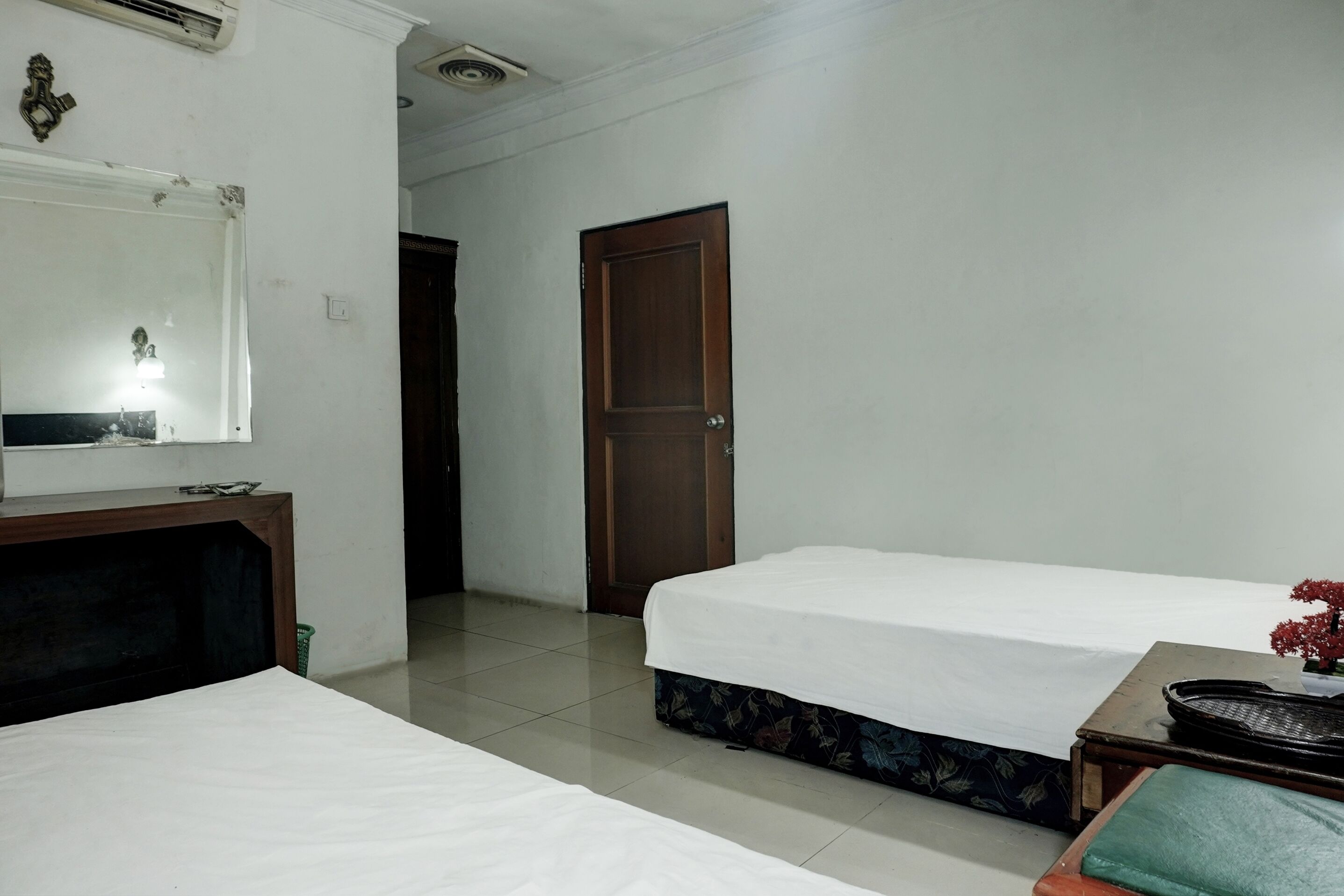Een hotelkamer met twee bedden, een houten bureau, een spiegel en een deur.