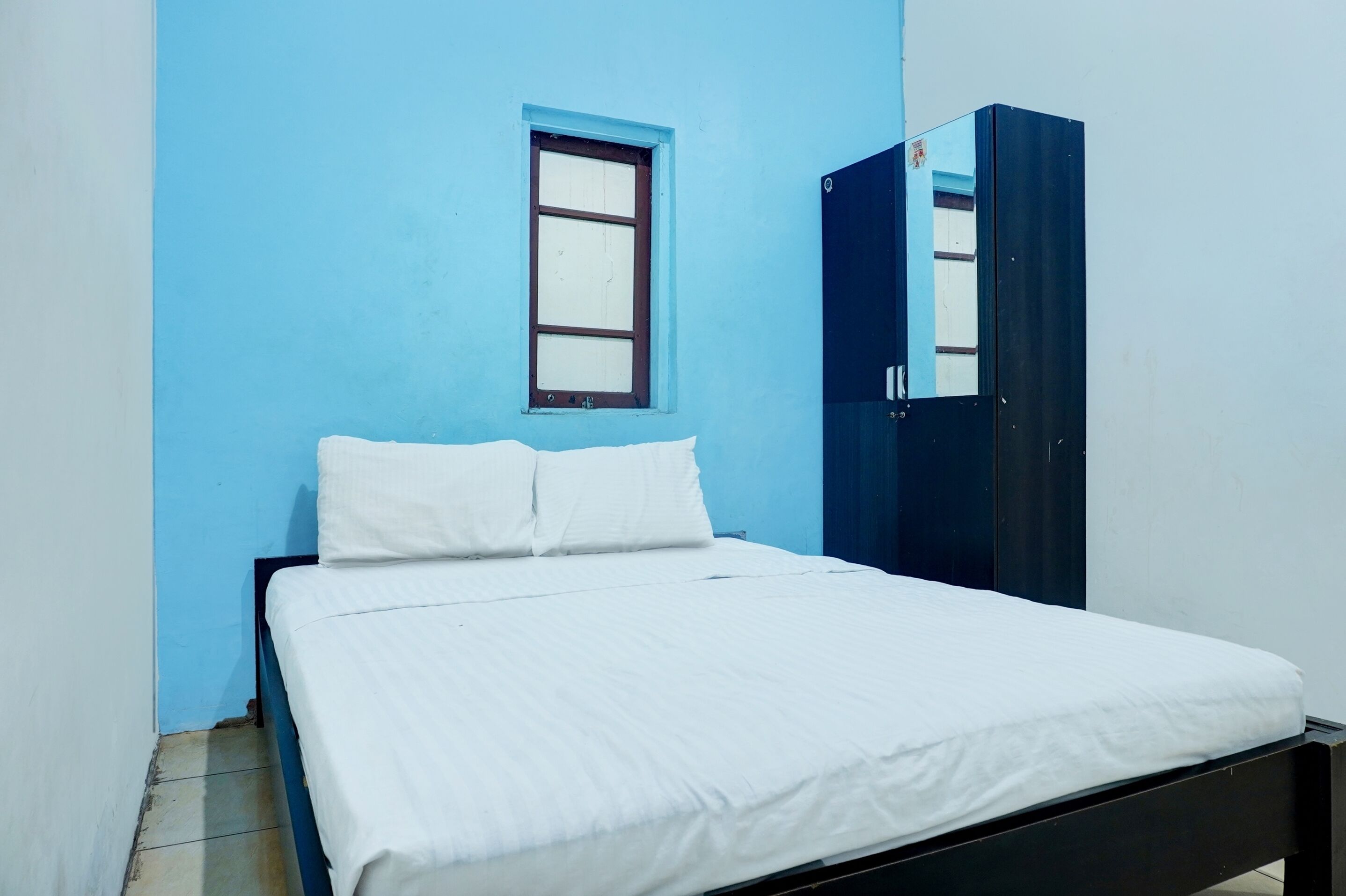 Uma cama de solteiro com roupa de cama branca num quarto com paredes azuis e uma pequena janela.
