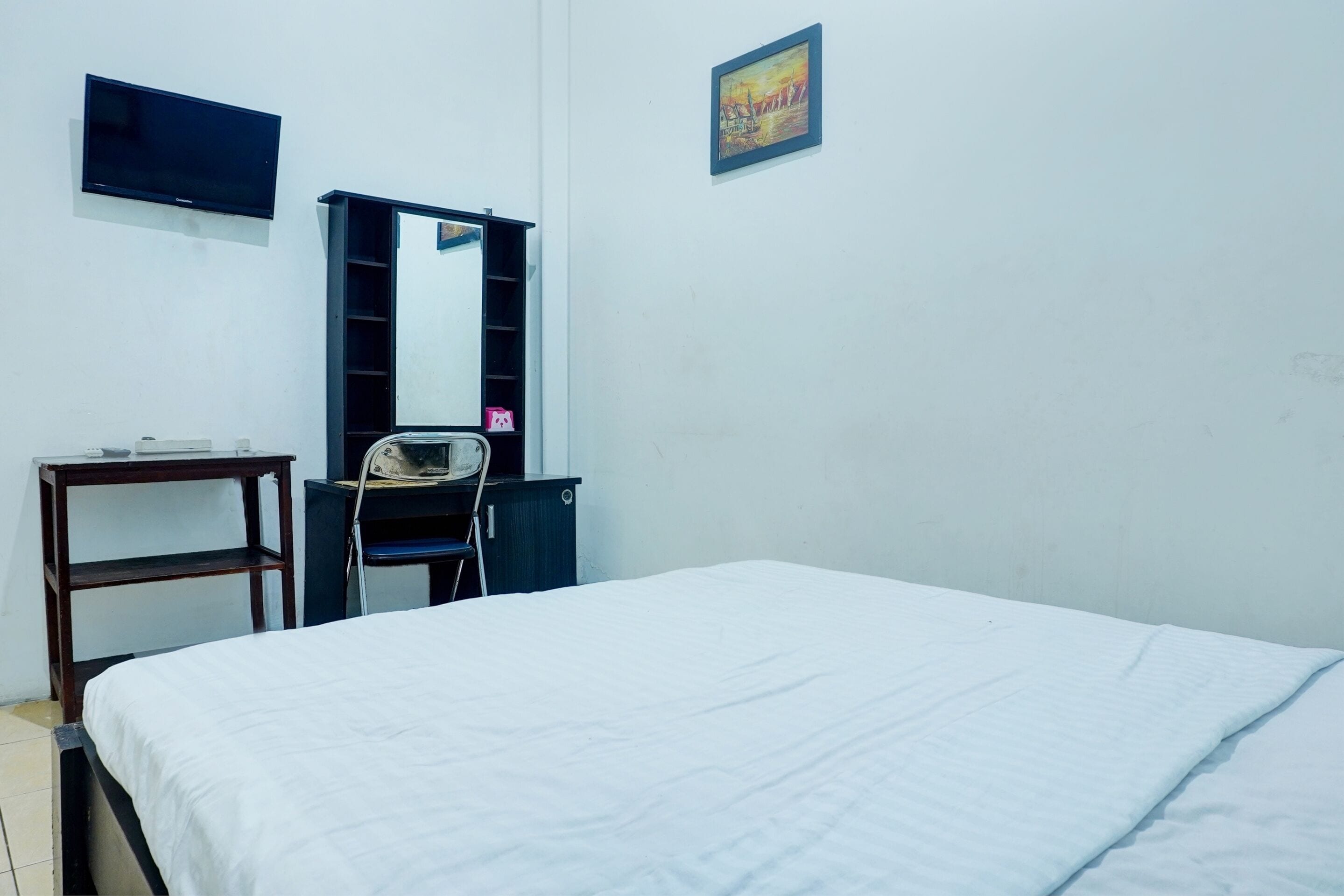 Une chambre à coucher comprenant un lit, un téléviseur fixé au mur, un bureau avec une chaise et un miroir.