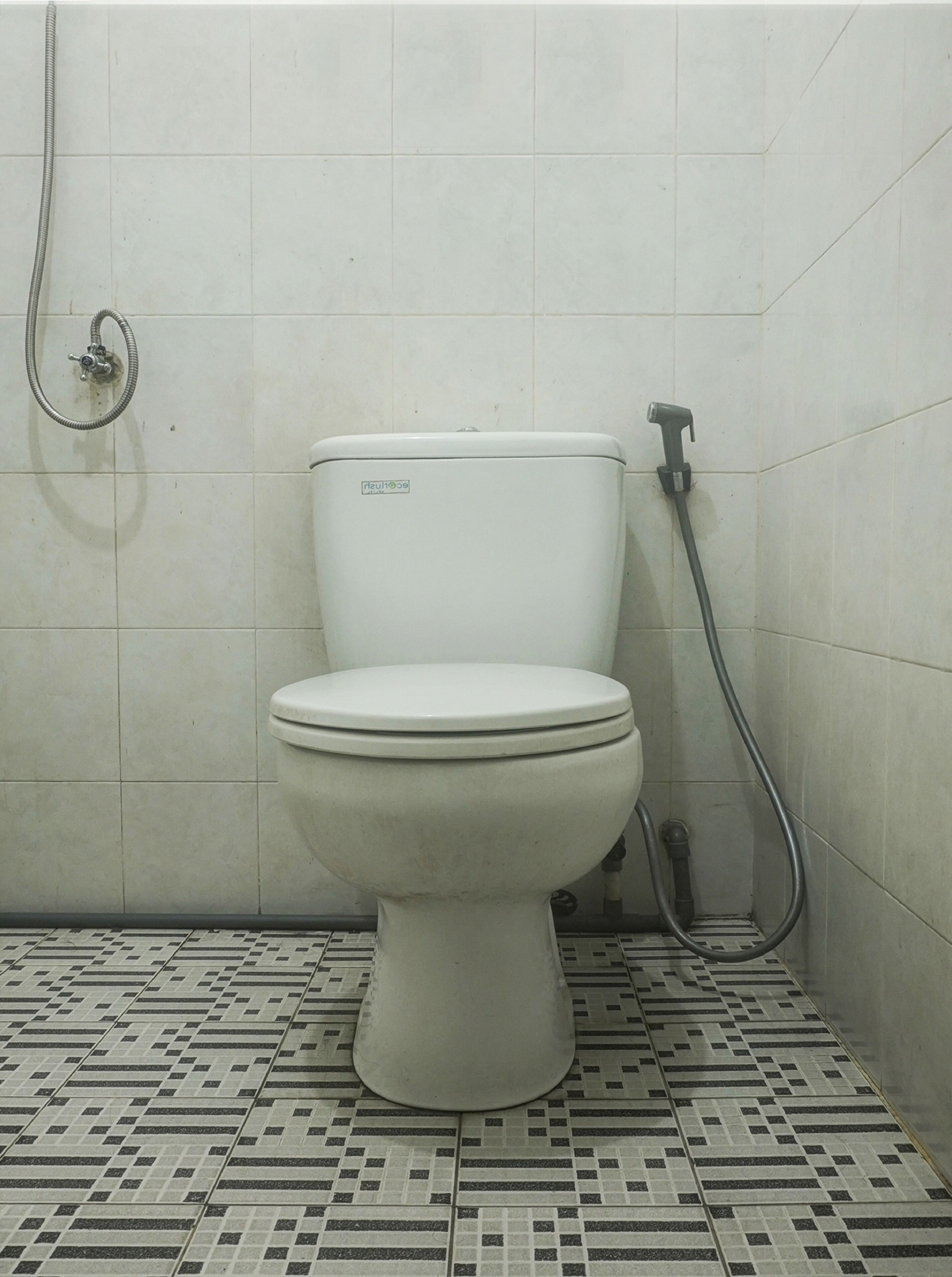 A toilet in a bathroom with a patterned floor and a shower hose.
