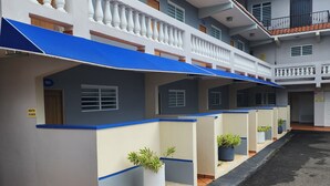 Un hôtel à plusieurs étages doté de balcons, de plantes en pot et d’une cour dallée.