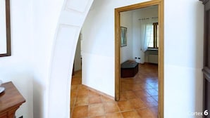 A corridor with a wooden door leading to a room with a tiled floor and a bench. - Villa Presaccia, ground floor apartment (Portoferraio)