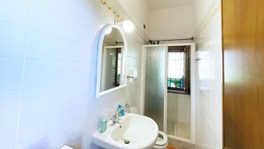 A bathroom with white tiles, a sink, a mirror, and a shower enclosure. - Villa Presaccia, ground floor apartment (Portoferraio)