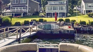 A boat docked at a marina with a view of a large house with a balcony and a lawn.