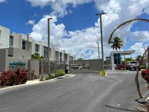 A modern building with a gated entrance, a clear sky, and a palm tree. - Beautiful 3bed/2bath with King Beds, 2 Pools, Gym & Full Generator, near beach! (Carolina)