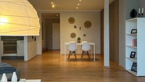 Moderni olohuone, jossa on valkoinen sohva, ruokapöytä ja kaksi tuolia, harmaa matto ja kirjahylly.