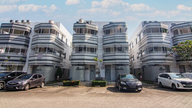 A modern building with multiple balconies and a parking lot with several cars. - Hotel O Anartha Residence (Pagedangan)