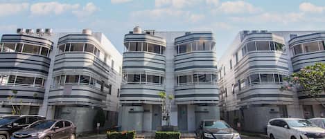 Un edificio moderno con varios balcones y un estacionamiento con varios coches.