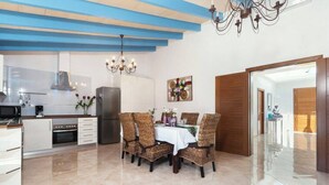 A modern kitchen with white cabinets, a stainless steel refrigerator, and a dining area with wicker chairs and a white tablecloth. - ,,,,,kkkkkkkkkkkkkk (Petra)
