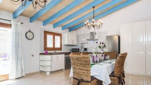 A modern kitchen with white cabinets, a stainless steel refrigerator, and a dining area with wicker chairs and a white tablecloth. - ,,,,,kkkkkkkkkkkkkk (Petra)