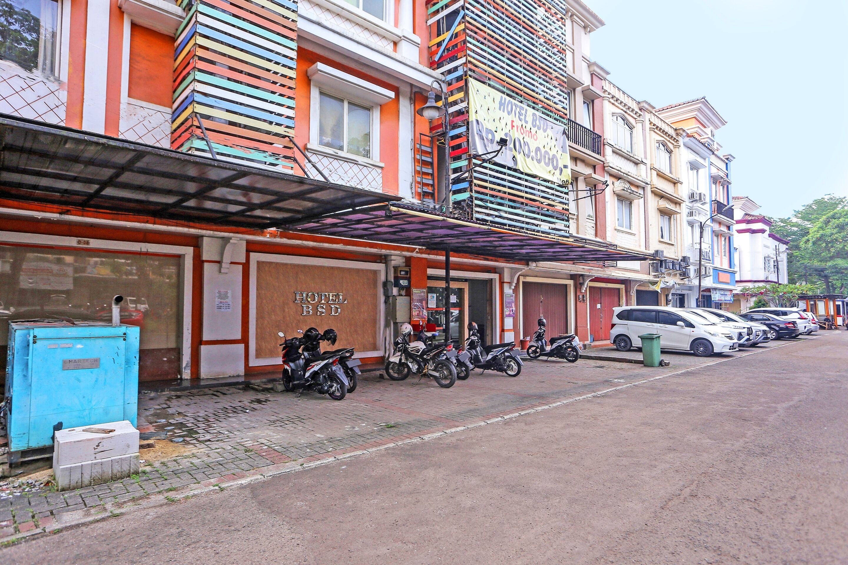 A hotel with a signboard, parked motorcycles, and cars along the street.