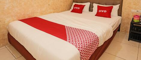 Una cama bien hecha con una colcha roja y blanca, dos almohadas rojas con la palabra 'OYO' bordada, y un cabecero de madera.
