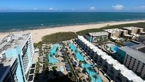 Ein Resort mit mehreren Schwimmbecken, Blick auf einen Strand und einem strahlend blauen Himmel.