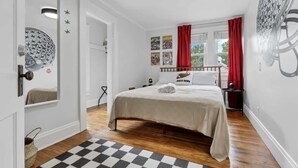A bedroom with a bed, a checkered rug, a window with red curtains, and wall decorations. - The Ohio State of Mind - OSU-Themed 5BR Home in Clintonville (Columbus)