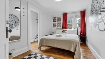 A bedroom with a bed, a checkered rug, a window with red curtains, and wall decorations.