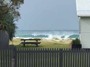 Vista sulla spiaggia con una panchina di legno, una recinzione e un edificio sullo sfondo.