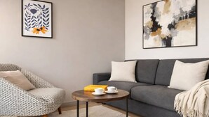 A living room with a grey sofa, a patterned armchair, a round coffee table with cups and a book, and two framed artworks on the wall. - Cosy studio - Eiffel Tower & Invalides (Paris)