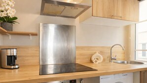 A modern kitchen with stainless steel appliances, a built-in oven, a washing machine, and wooden cabinetry. - Cosy studio - Eiffel Tower & Invalides (Paris)