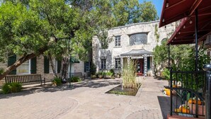 A courtyard with a stone pathway, a building with a sign reading 'HOBBY HOUSE,' and a covered area with plants. - Romantic 1BR Suite on Main Street / Prime location (Fredericksburg)