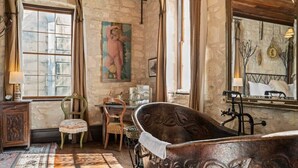 A rustic room with a vintage bathtub, a wooden chair, a table with a lamp, and a large window with curtains. - Romantic 1BR Suite on Main Street / Prime location (Fredericksburg)
