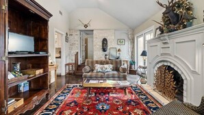 Een woonkamer met een open haard, een bank, een bijzettafeltje en een groot vloerkleed.