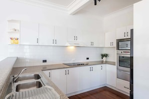 Una cocina moderna con armarios blancos, un lavamanos de acero inoxidable y un horno empotrado.