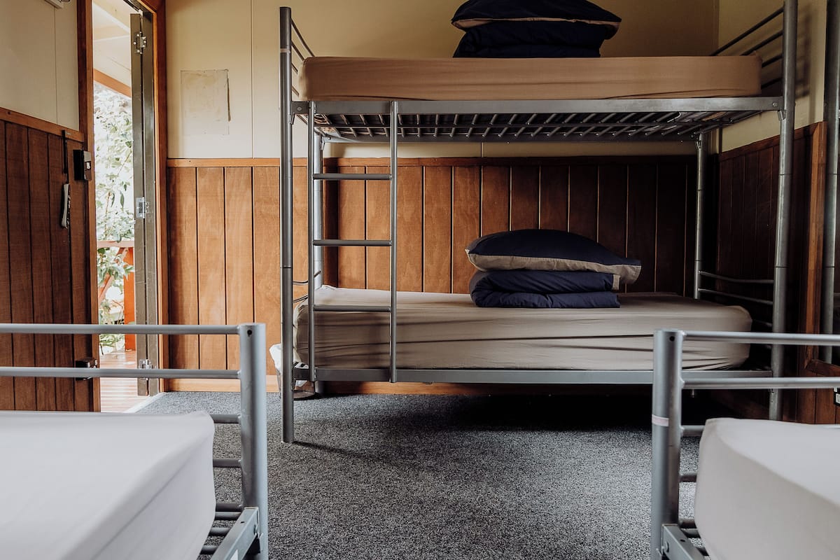 A bunk bed room with a wooden wall, a metal ladder, and a small window.