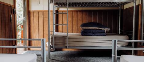 Dormitorio con literas, una pared de madera, una escalera de metal y una ventana pequeña.