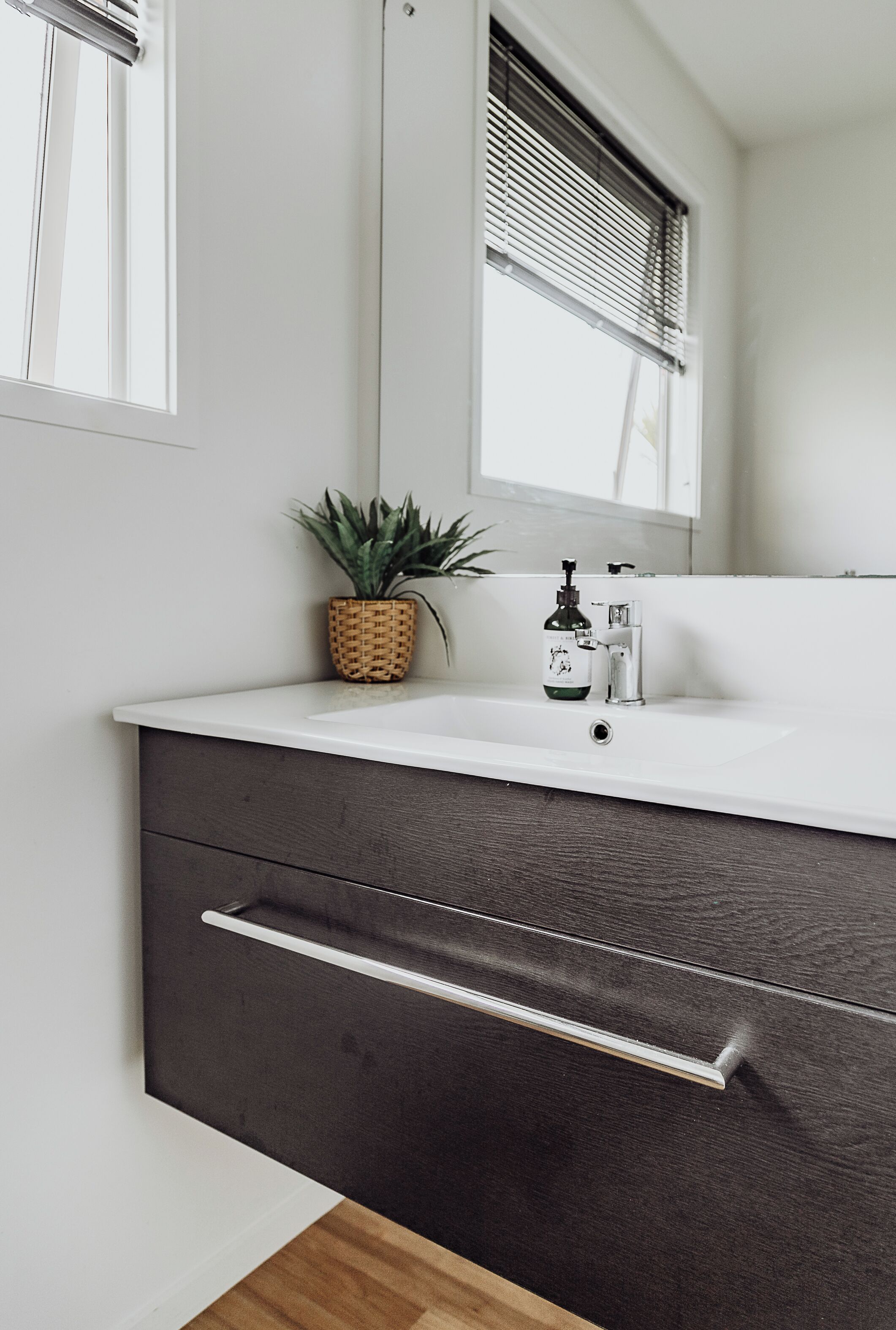 A bathroom with a white sink, dark wooden cabinet, and a potted plant.