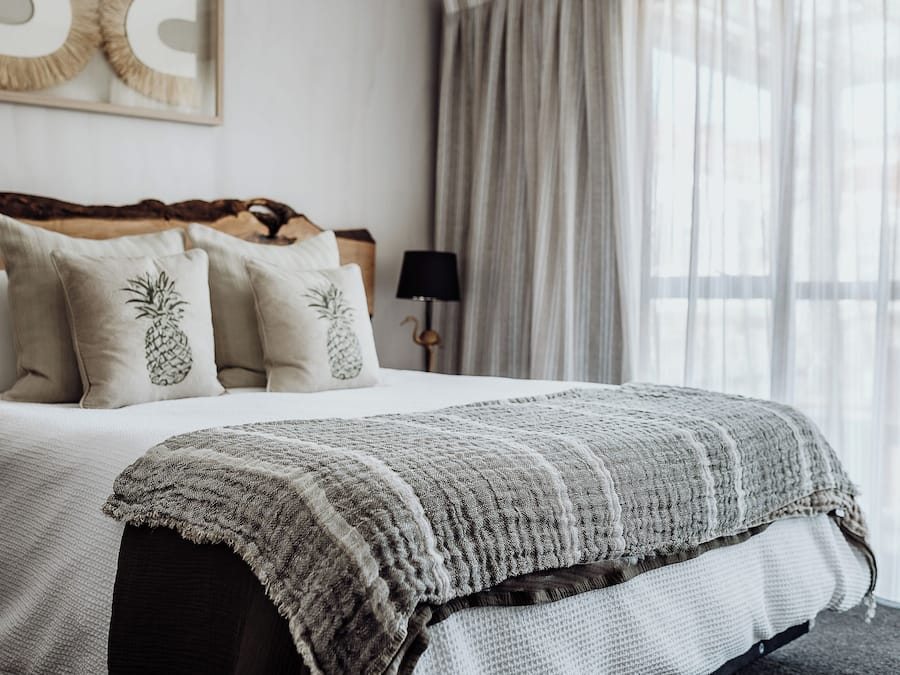A neatly made bed with a striped blanket, two pineapple pillows, and a wooden headboard.