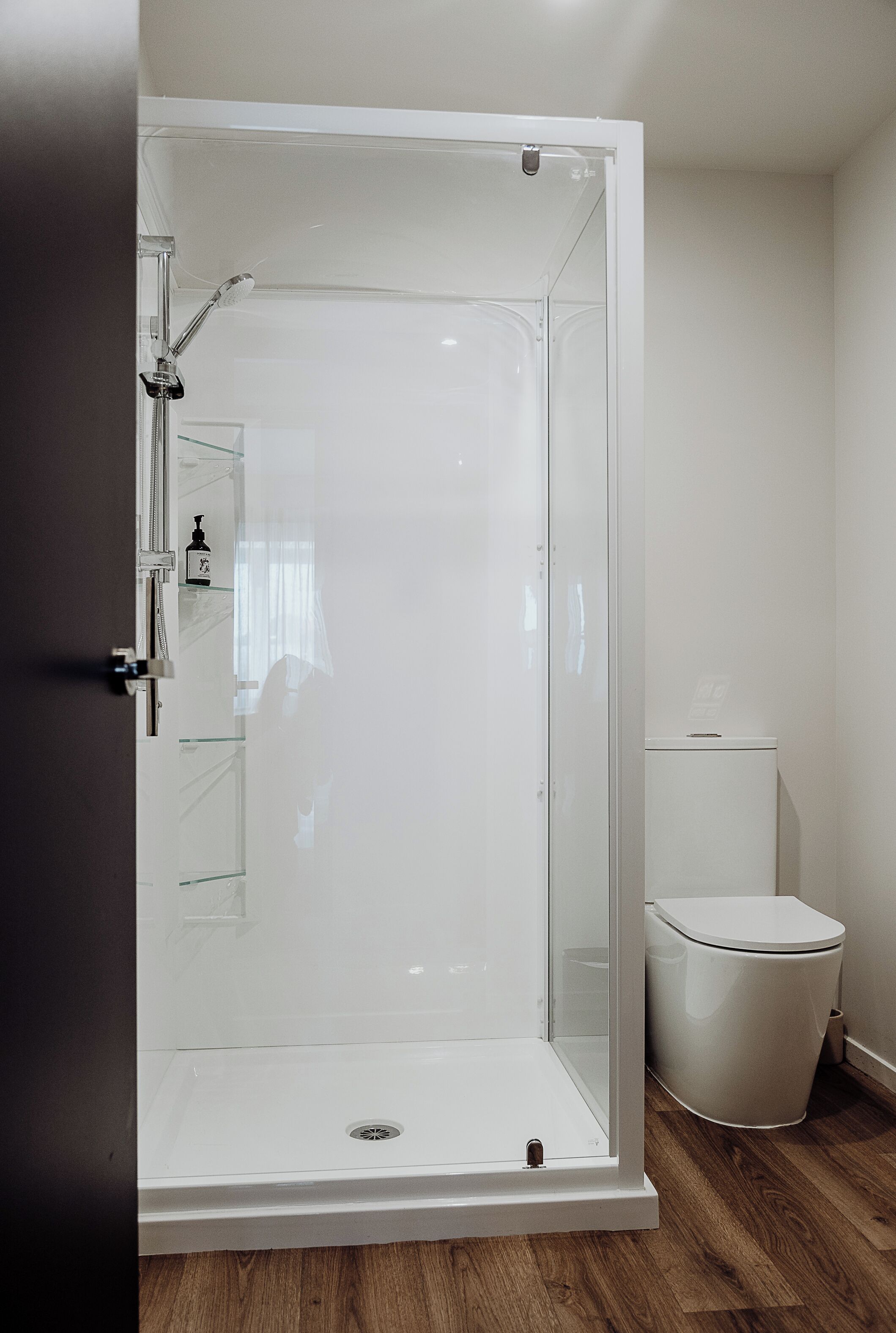 Une salle de bain moderne avec une douche à parois de verre, des toilettes et une petite étagère contenant des articles de toilette.