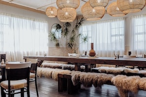 A dining area with a long wooden table, multiple chairs, and benches with fur throws. - Lake Mahinapua Hotel (Ruatapu)