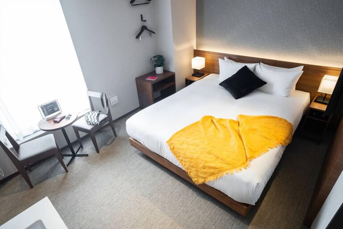 A hotel room with a bed, bedside tables, a desk with a chair, and a small table with a plant.