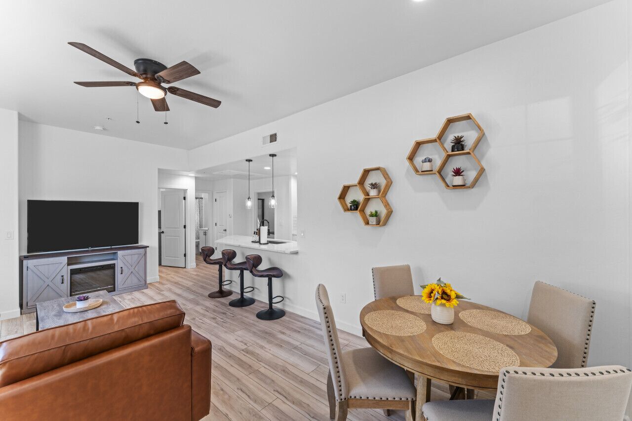 A modern living room with a flat-screen TV, leather sofa, and a dining area with a wooden table and chairs.